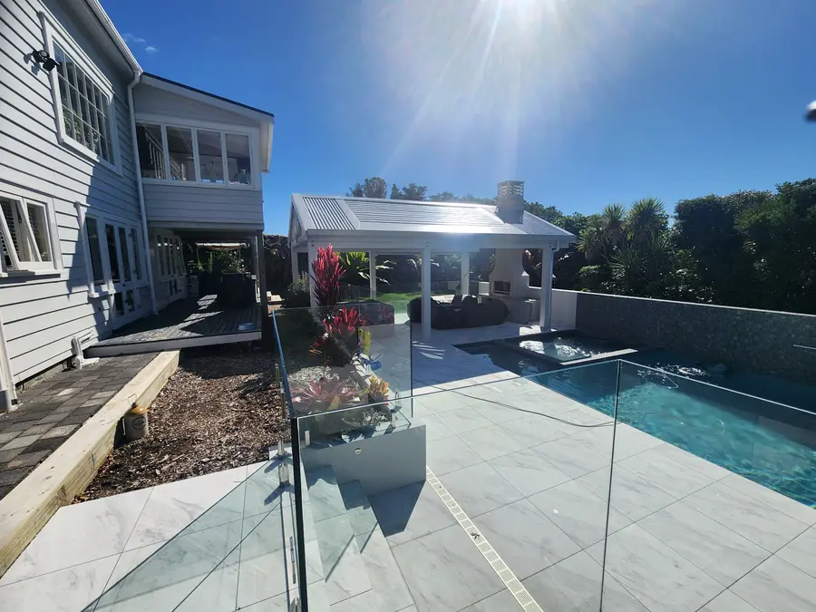 The pool, glass fence and pergola beside a white weatherboard house