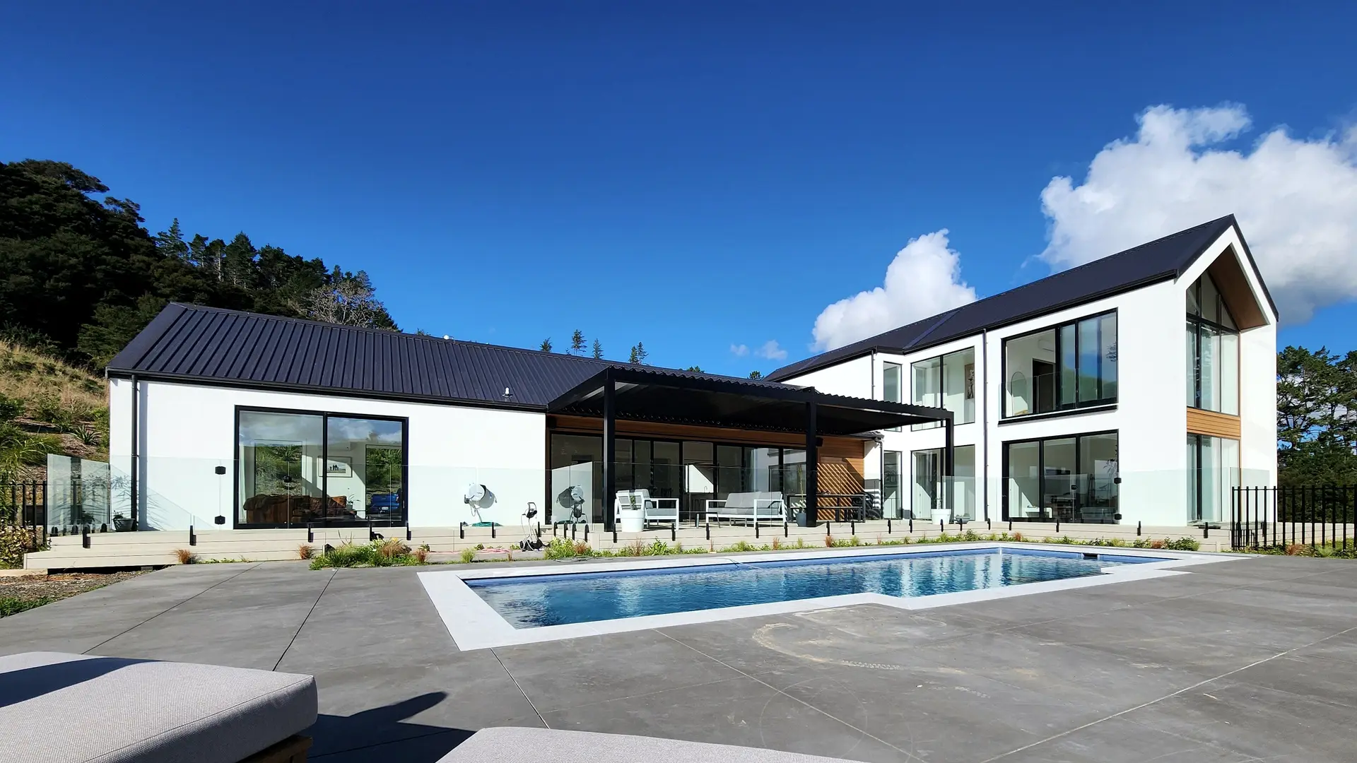 A finished two-storey white house with dark roof and a swimming pool in front
