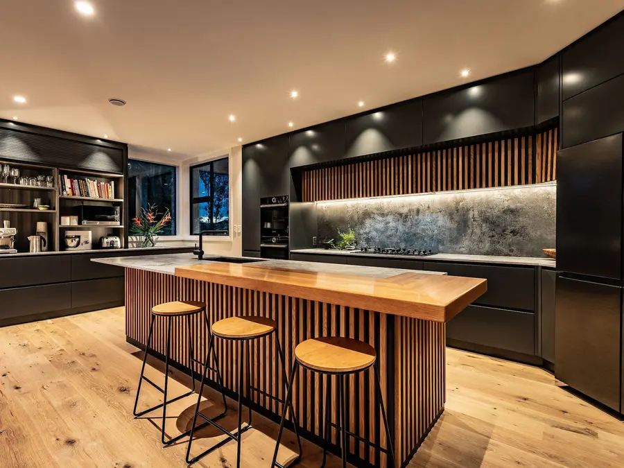 A new dark kitchen with a slatted timber island, stone benchtop and timber floors