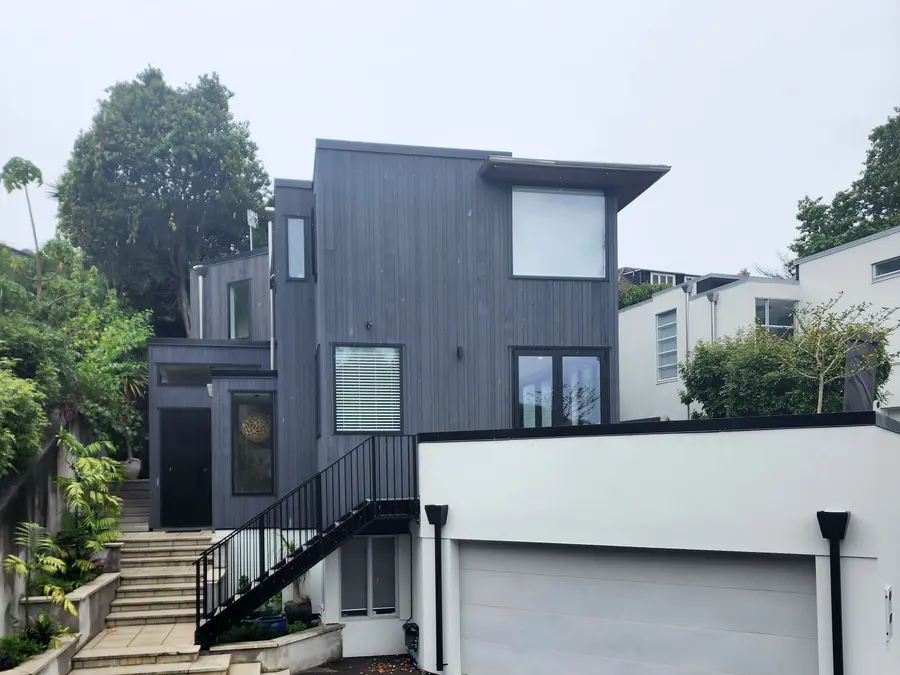 After: the house re-clad in dark vertical timber with a white garage